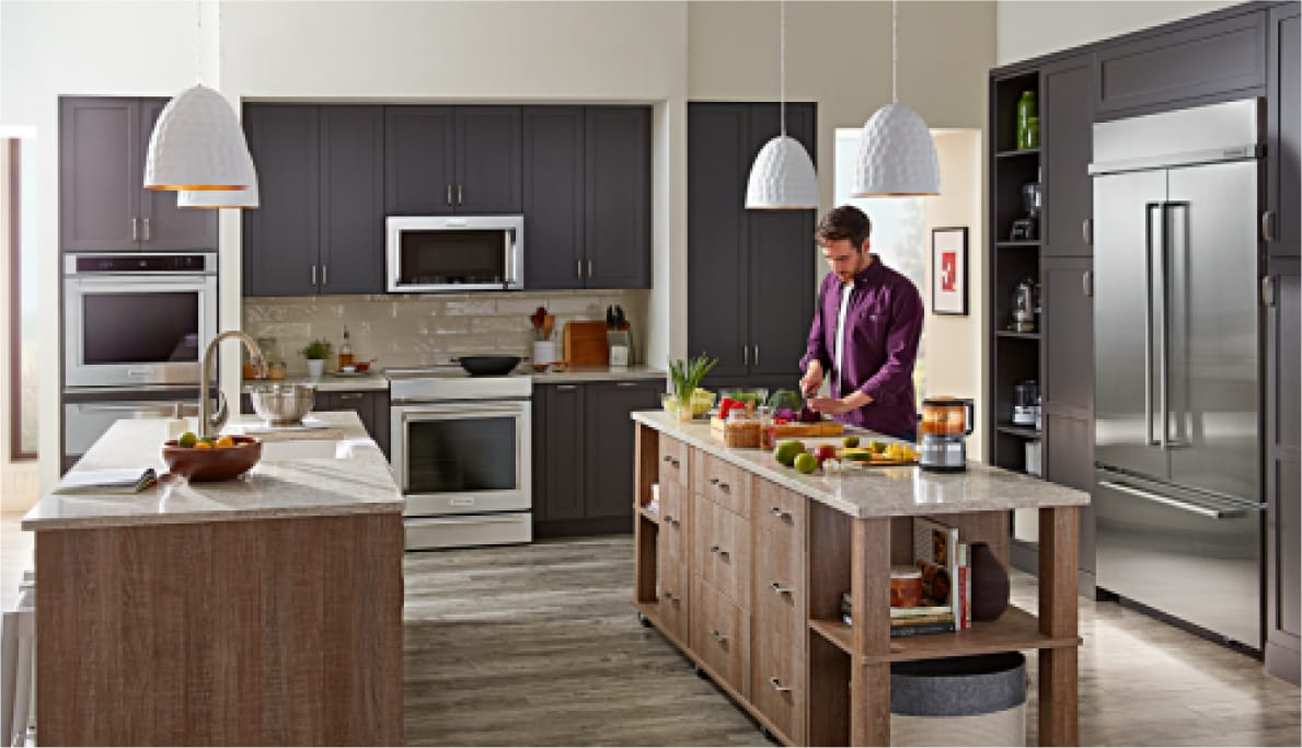 A person cooking at one of the double islands in a kitchen filled with KitchenAid® appliances.