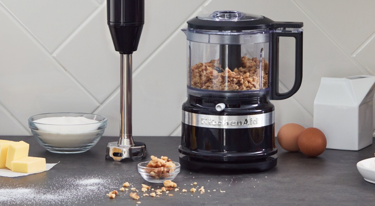 Black KitchenAid® food processor filled with walnuts sitting next to an upright immersion blender on a counter Black KitchenAid® food processor filled with walnuts sitting next to an upright immersion blender on a counter