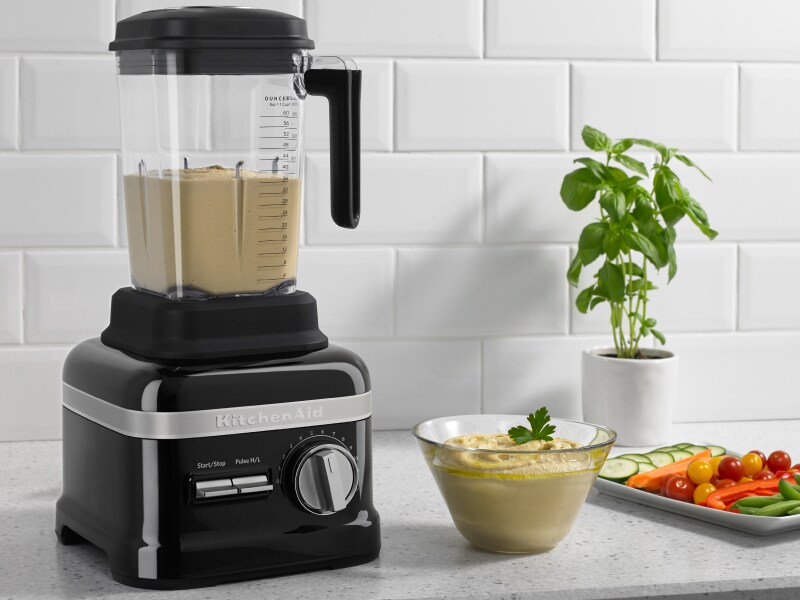 A KitchenAid® blender with hummus on a modern kitchen counter next to fresh vegetables. A KitchenAid® blender with hummus on a modern kitchen counter next to fresh vegetables.
