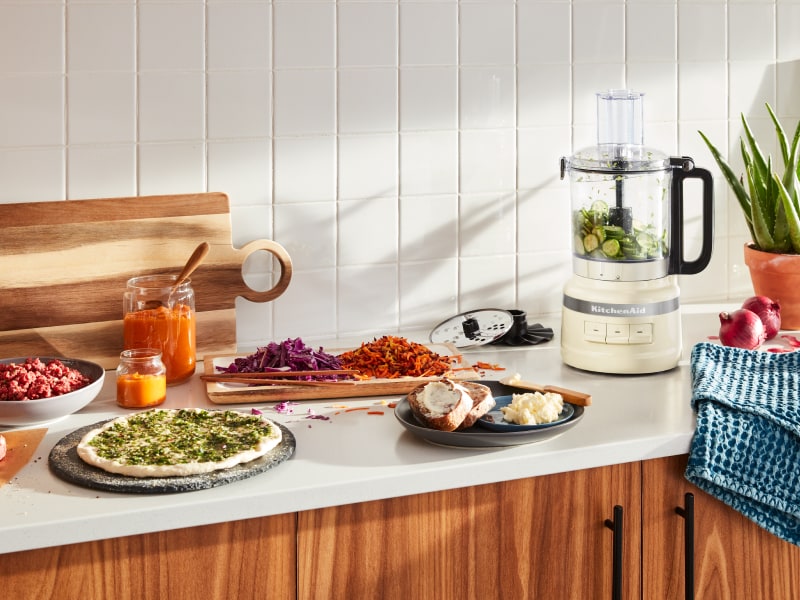 A KitchenAid® food processor with fresh vegetables in a modern kitchen. A KitchenAid® food processor with fresh vegetables in a modern kitchen.