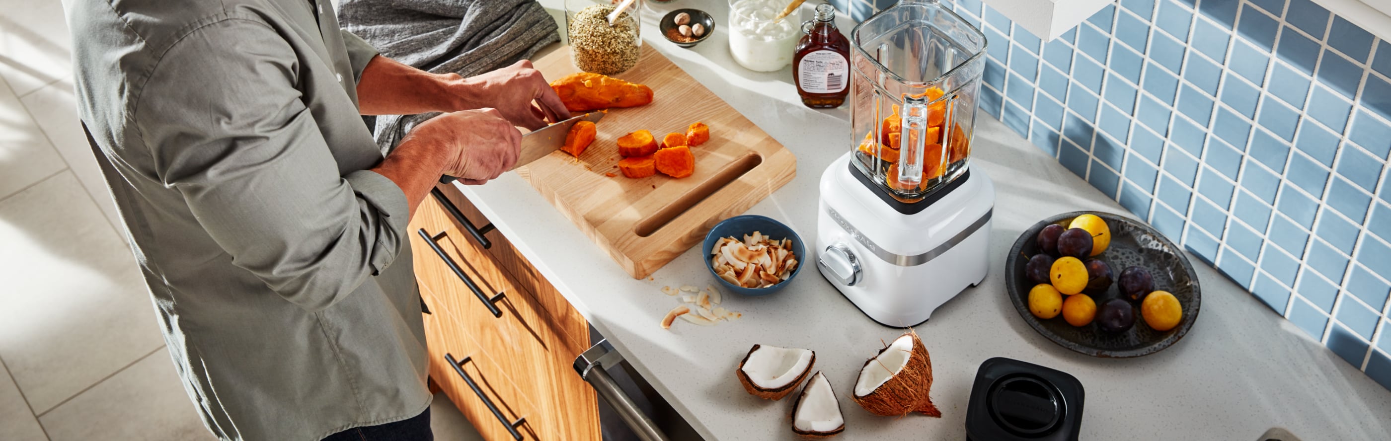 A man in a modern kitchen cutting vegetables to add to a KitchenAid® blender.