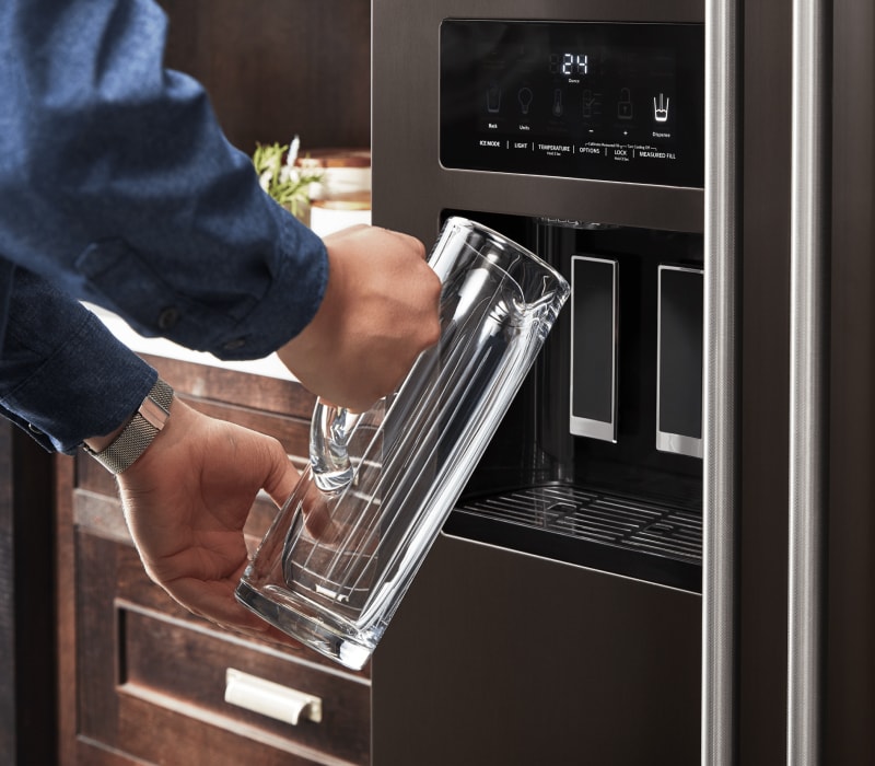 Man filling a tall glass mug with water from a fridge water dispenser