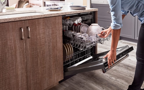 Hands opening a top control built-in dishwasher next to wood grain cabinets