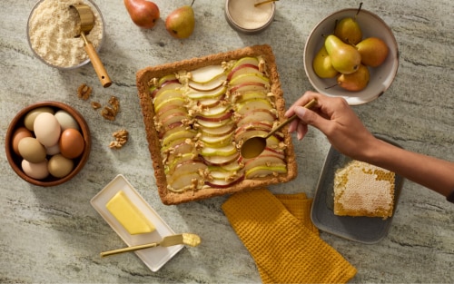 Person spooning honey onto a pear dessert