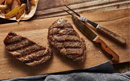 Steak resting on a cutting board next to a bowl of chimichurri sauce