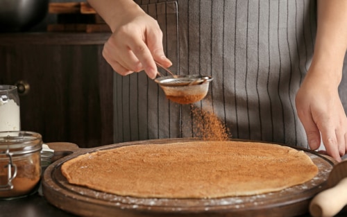 Person dusting dough with sifted cinnamon