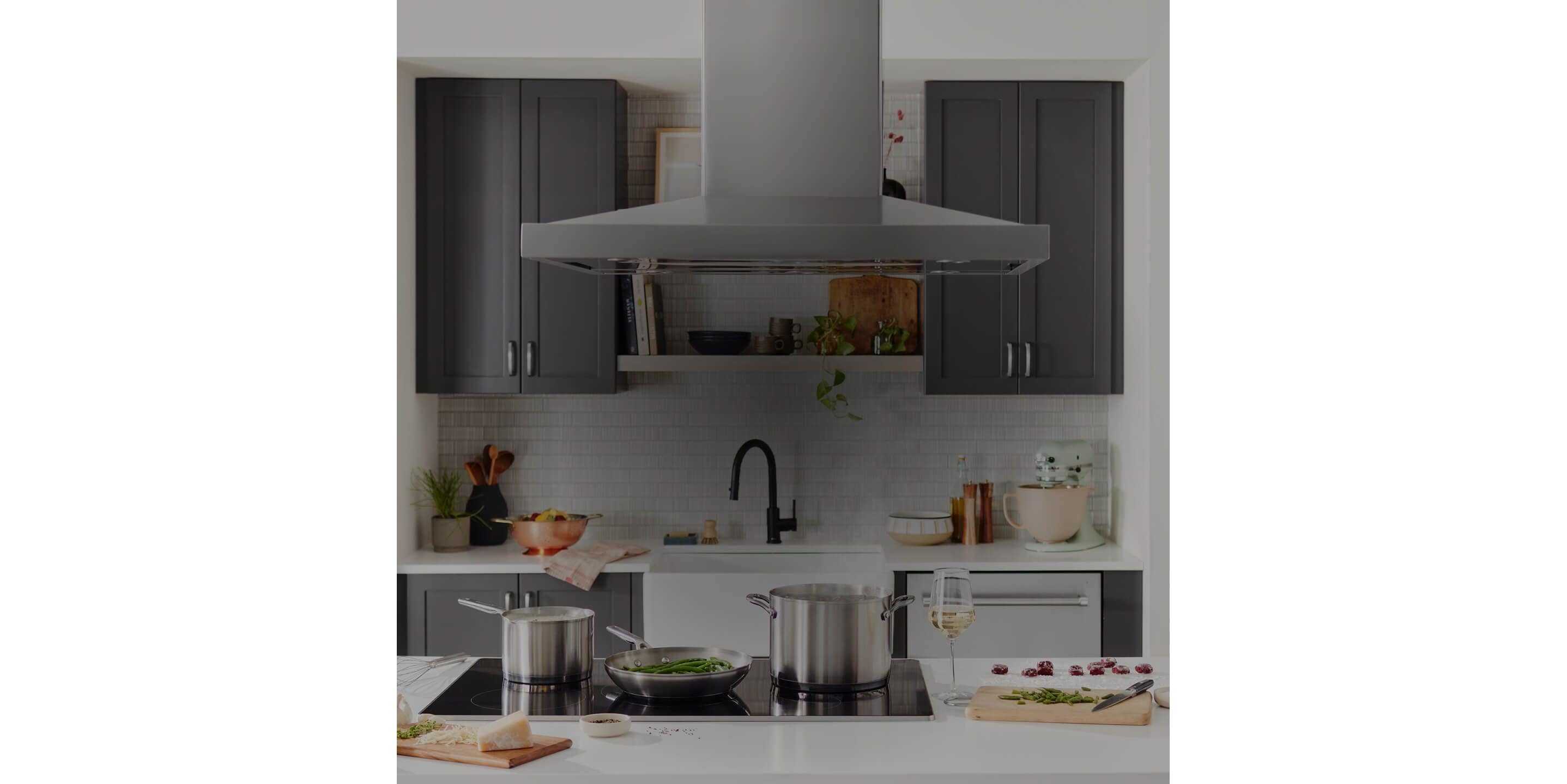 A ventilation hood above a cooktop with several tall saucepans on it.