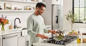 A person cooking on a KitchenAid® cooktop.